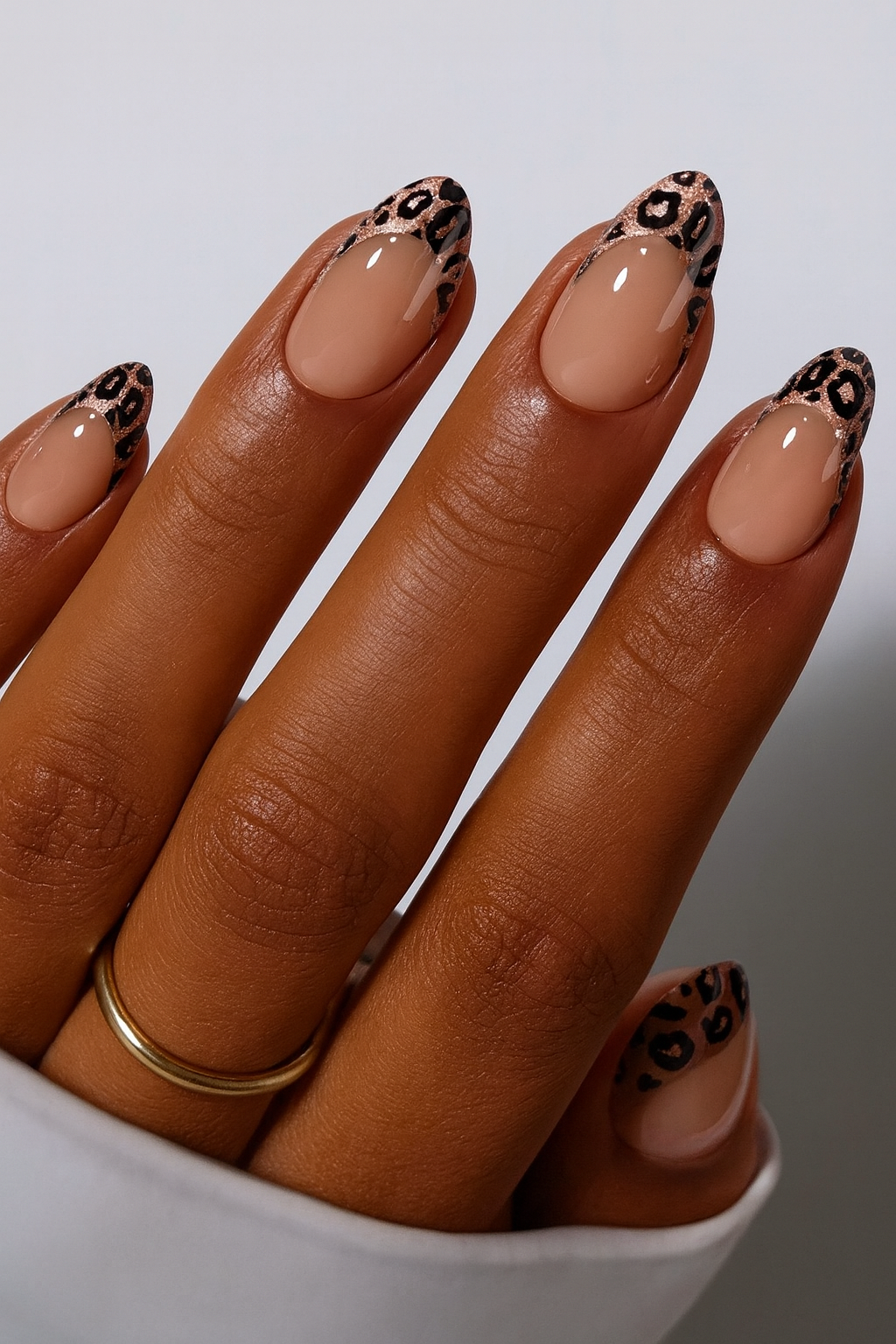 Hand with nude base and leopard print french tips on a white background