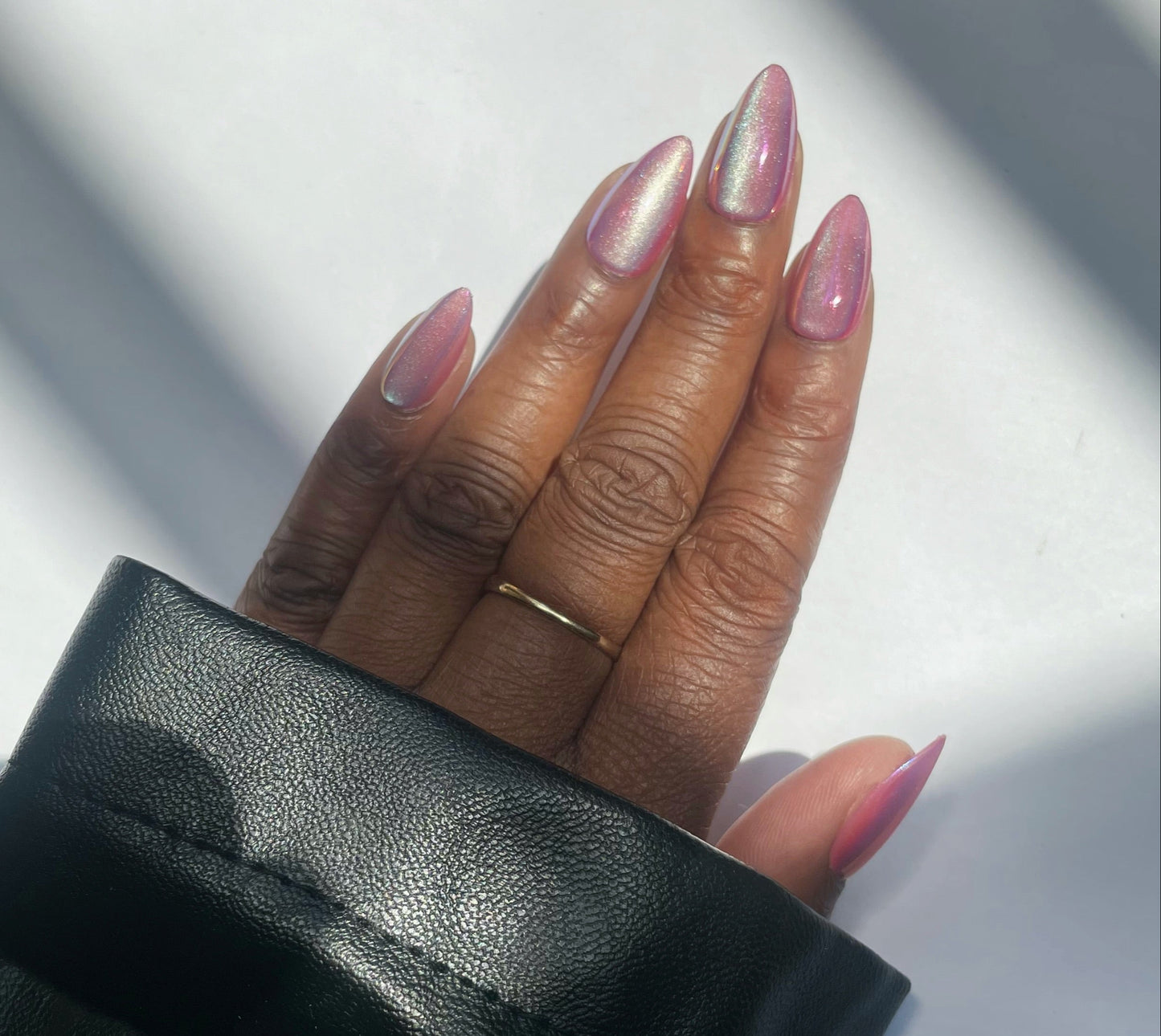Hand with pink chrome press on nails wearing a gold ring against a neutral background