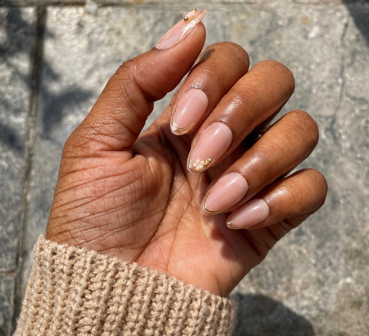 Camellia nude floral soft gel almond press-on nails with gold French tips on brown skin