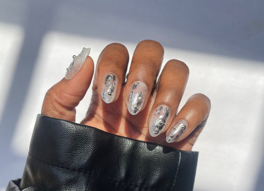 Hand wearing a black sleeve with silver nail art against a blurred background